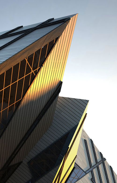 Close-up of a sharp, angular modern building facade with warm golden light reflecting on geometric window panels.